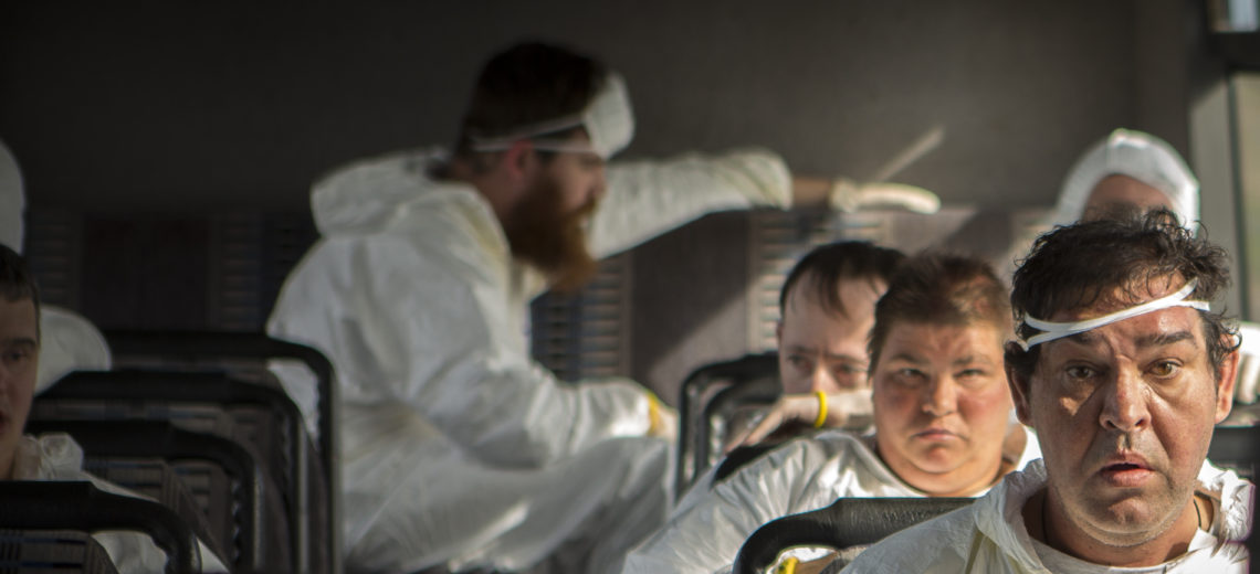 Six people are sitting on a bus wearing white overalls