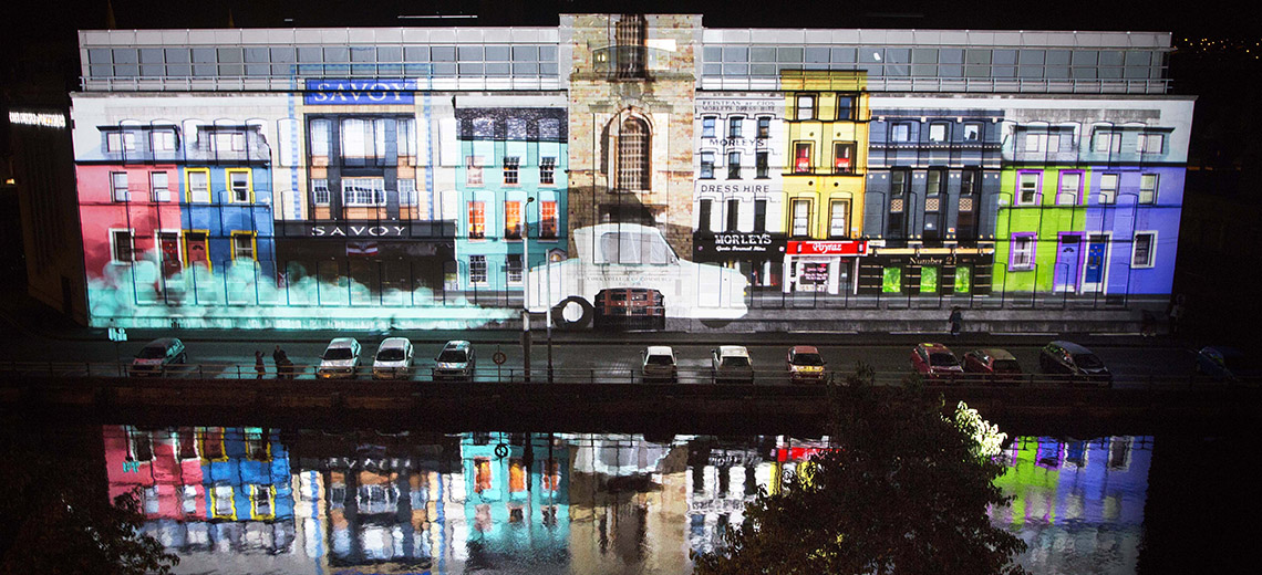 Light projection of colourful buildings onto a large building