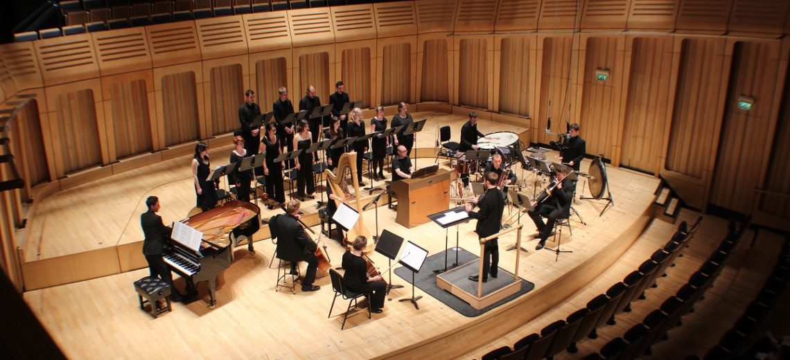 A conductor, orchestra and choir on a stage in an auditorium