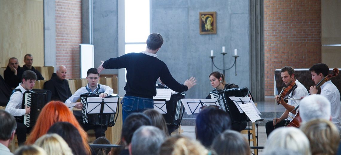 A man conducting a small orchestra in front of an audience. 