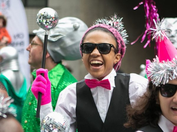 A group of performers outdoors, wearing tinsel covered party hats.