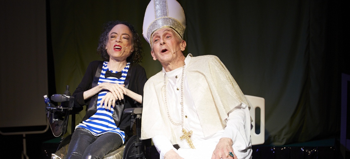 A woman in a power assisted chair next to a man dressed as a bishop.