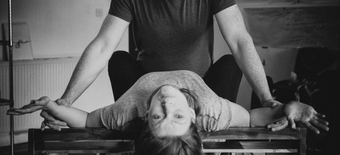 Woman lying on her back with her head bent back. A person is holding her arms. 