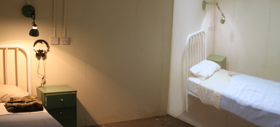  A bed with a cabinet, headphones and a wall light positioned next to a wall with a projection of the same image. 