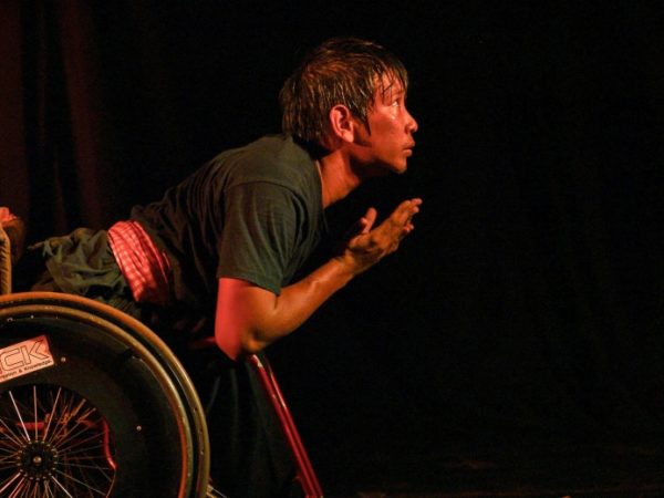 A performer in a wheelchair on a dark stage.