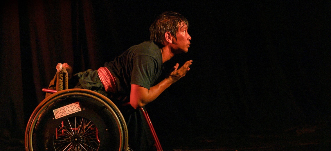 A performer in a wheelchair on a dark stage.