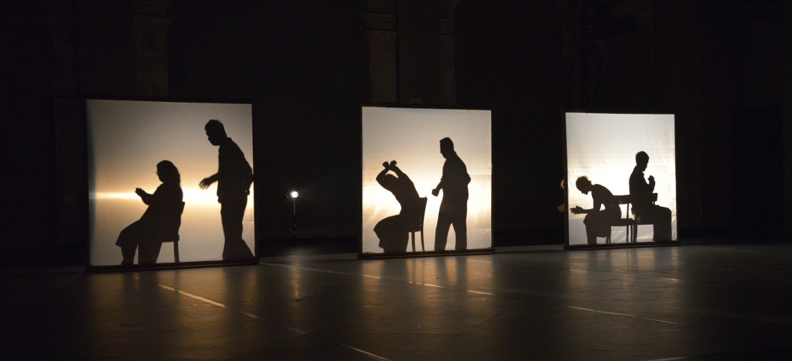 A silhouette of six performers behind back lit screens. 