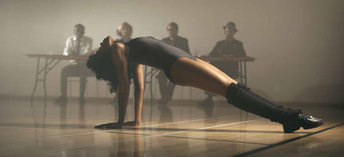 A dancer raising herself from her hands from the floor, looking towards the ceiling. 