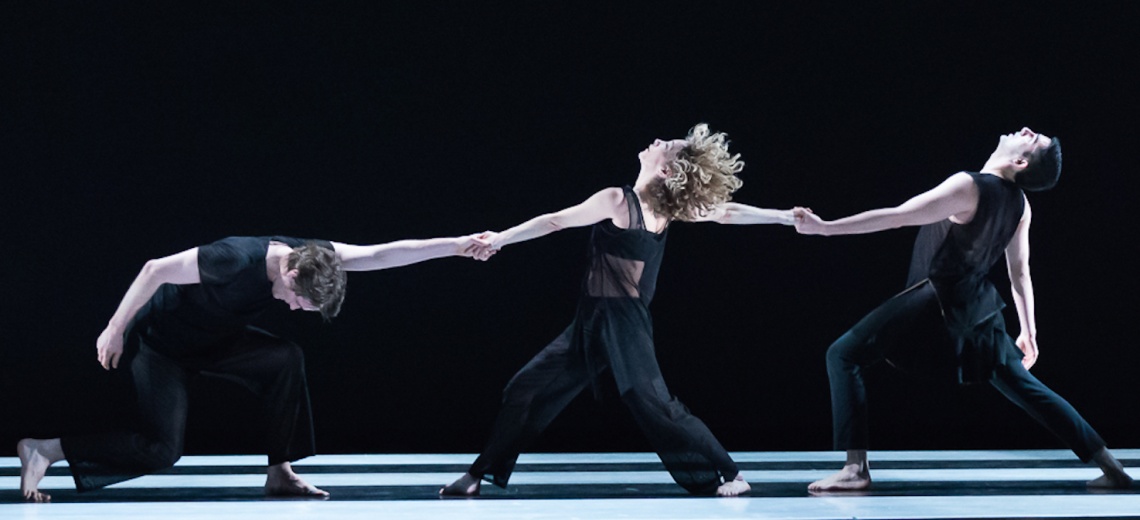 Three dancers on a stage with their arms outstretched and holding hands