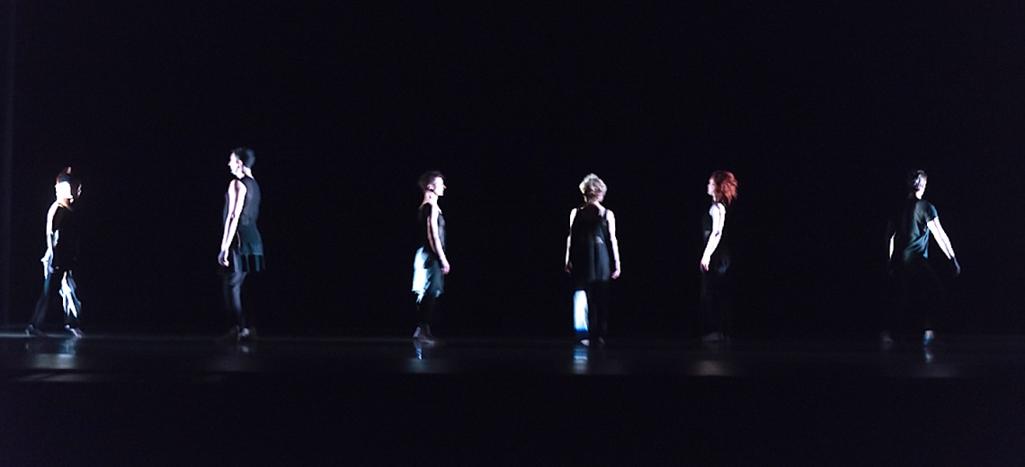 Six dancers at a distance, on a stage. 