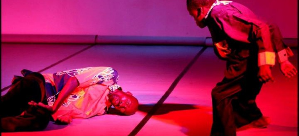 Two performers on a stage, in a conversation where one is lying down and the other with disability is standing 