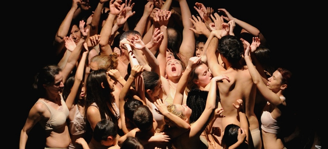 A group of performers on stage all crowded together with arms raised in the air