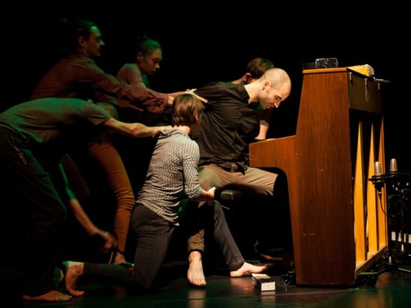 Five people appear to be pulling a person away from their seat at a piano