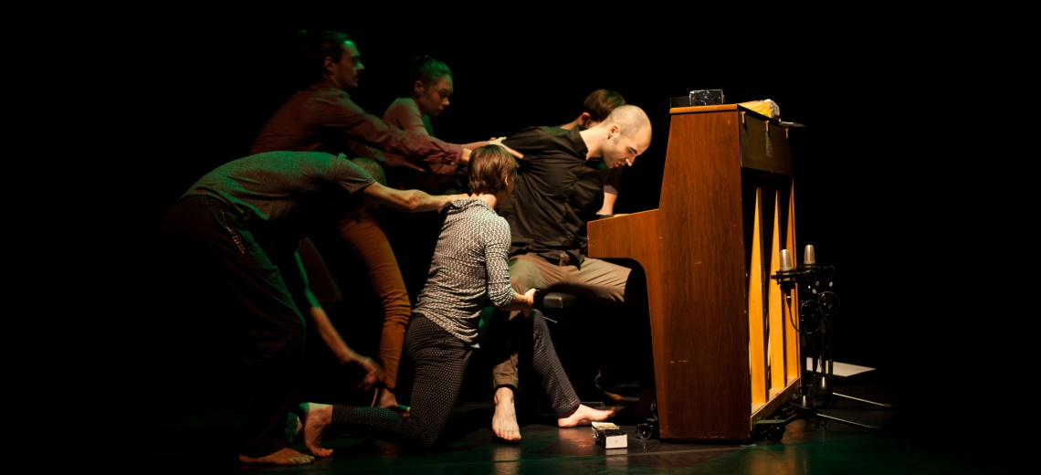 Five people appear to be pulling a person away from their seat at a piano