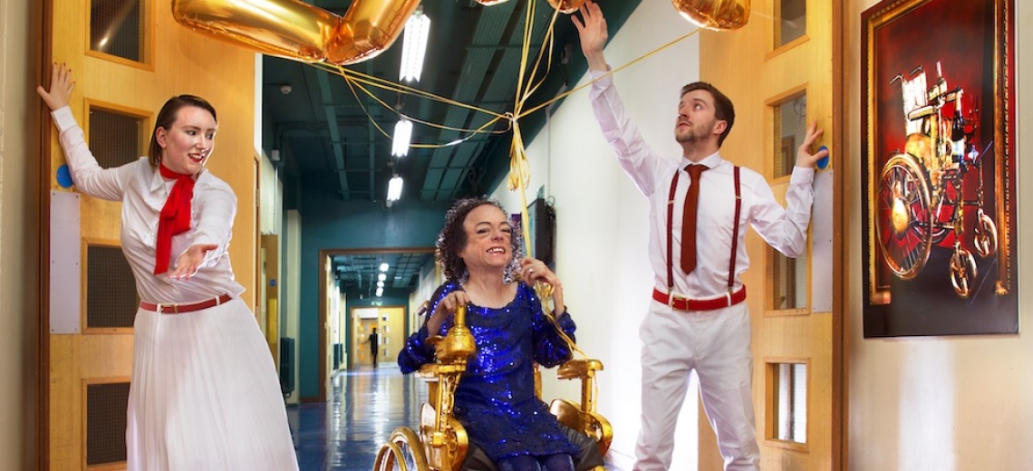 Three performers in a long corridor, one performer is in a power assisted chair.