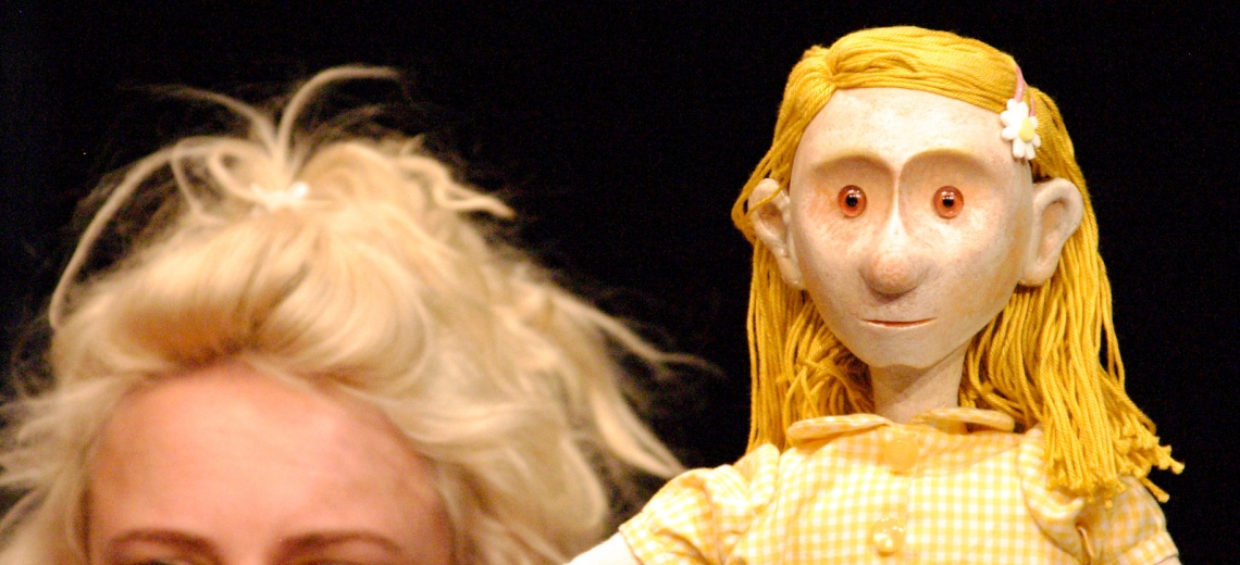 A puppet with yellow hair and dress next to a performer with blond hair.