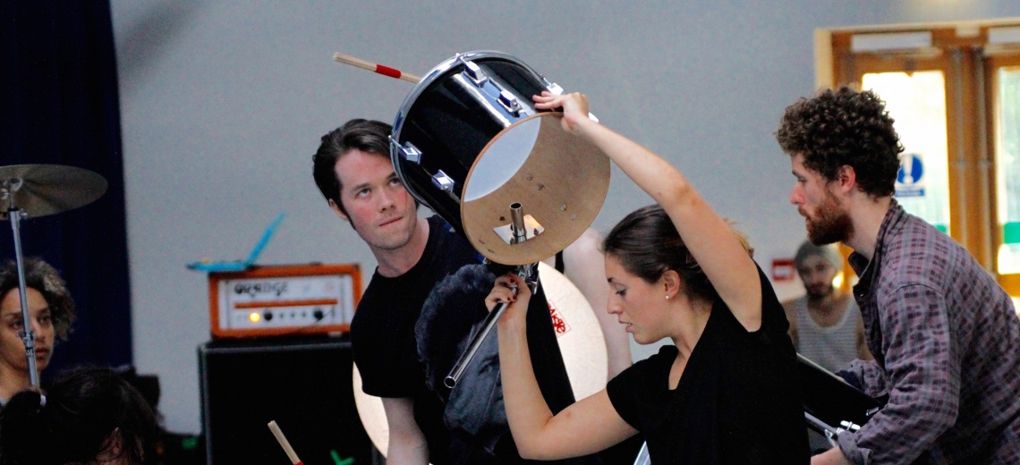 Five people in a room, one holding a drum in the air. 