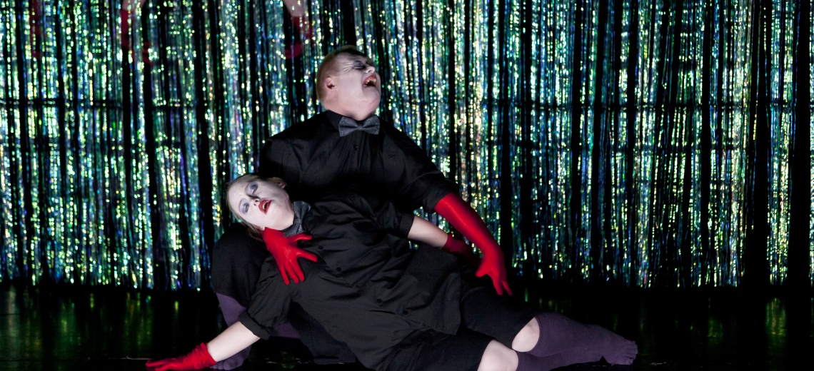 Two performers lying together on stage
