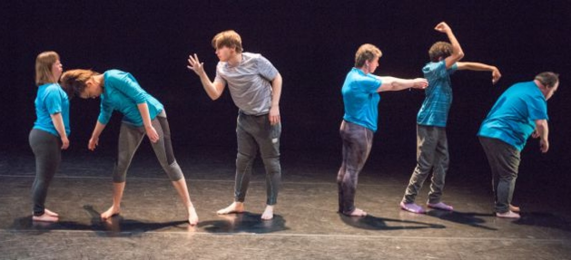  Six performers on a stage in a row, in a range of poses.