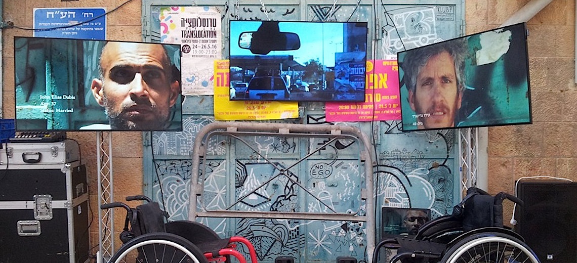  Two wheelchairs in front of a panelled wall and under three suspended television screens. 