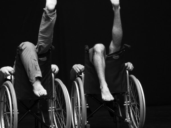 Two people sitting back to front in wheelchairs with their legs in the air.