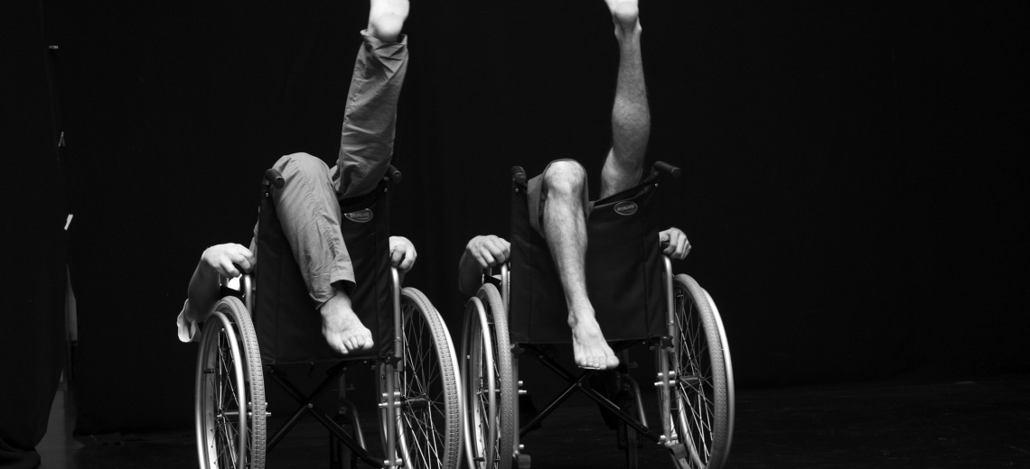 Two people sitting back to front in wheelchairs with their legs in the air. 