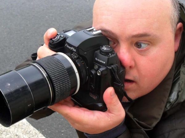 A man holding a long lens camera to his face, taking a photograph.