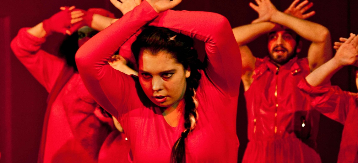 Four performers all with their hands crossed above their heads, dressed in red. 