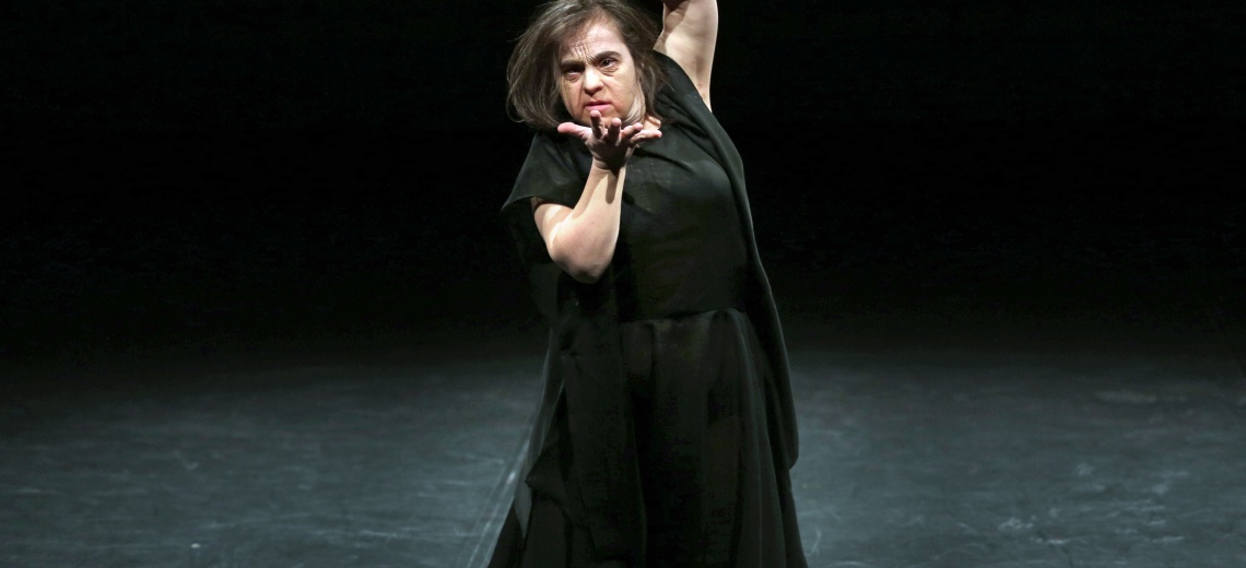 A single performer on the stage, her hands are making a gesture. 