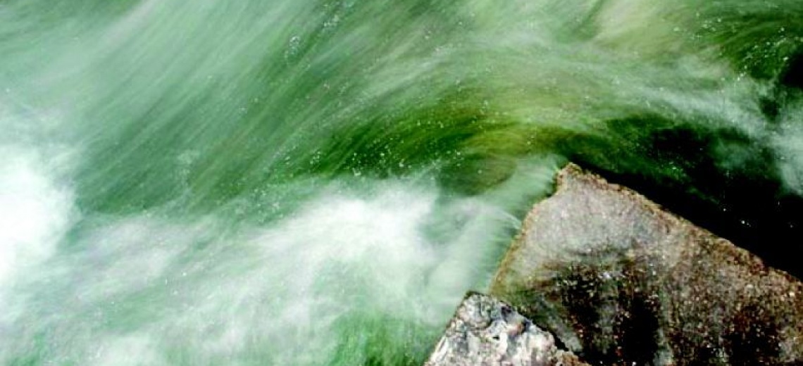 Swirling green and white water around a corner of stone.