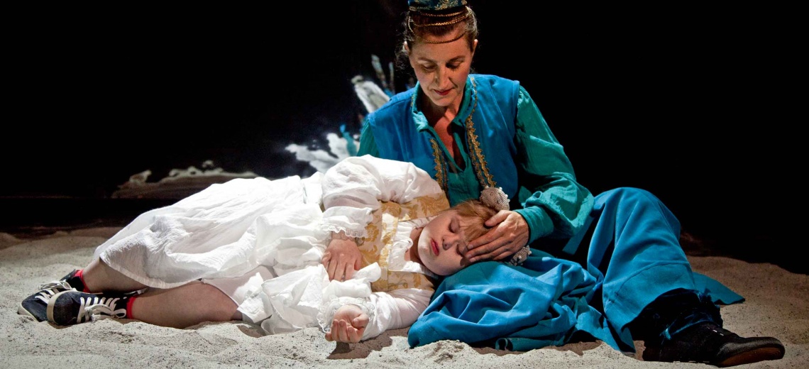 A performer lying on sand with her head in the lap of another. 