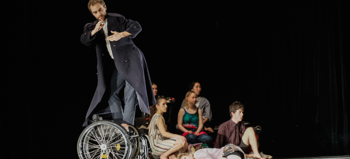 Performer standing on a wheelchair as 6 other performers stand behind him