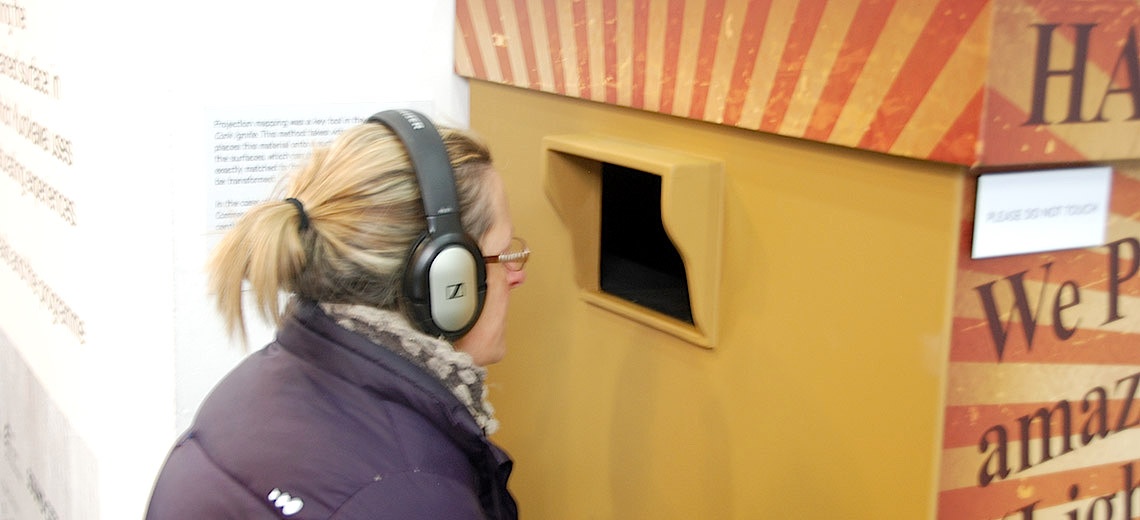 A woman wearing headphones looking into a yellow box. 