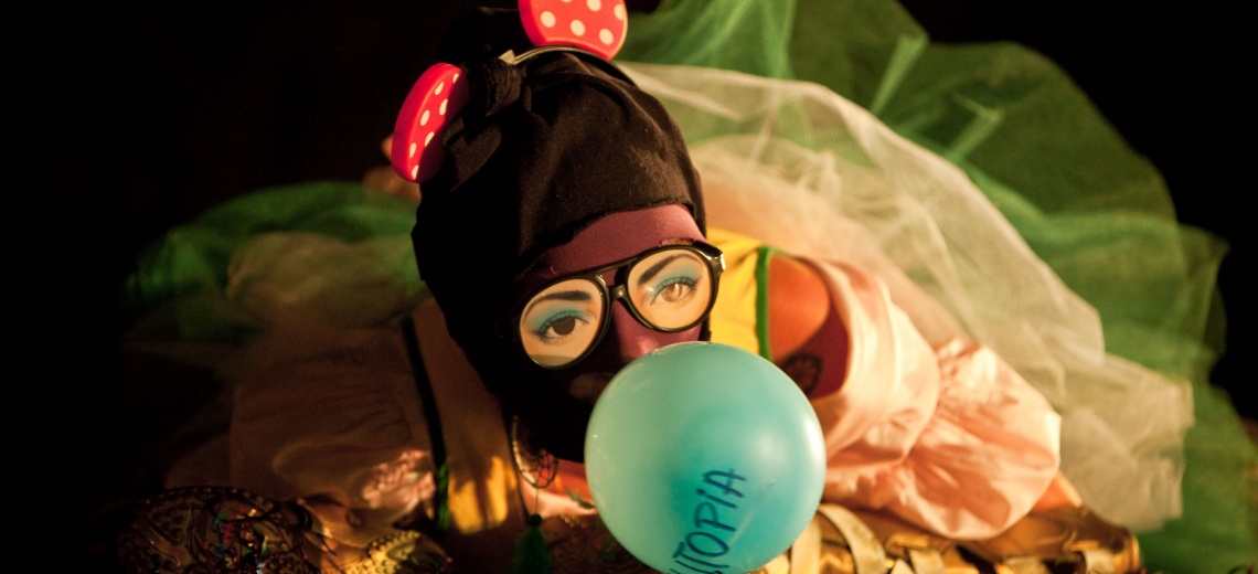 A person in a balaclava and large glasses blowing up a balloon.