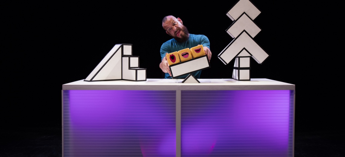 A performer sitting behind a desk on a stage. 