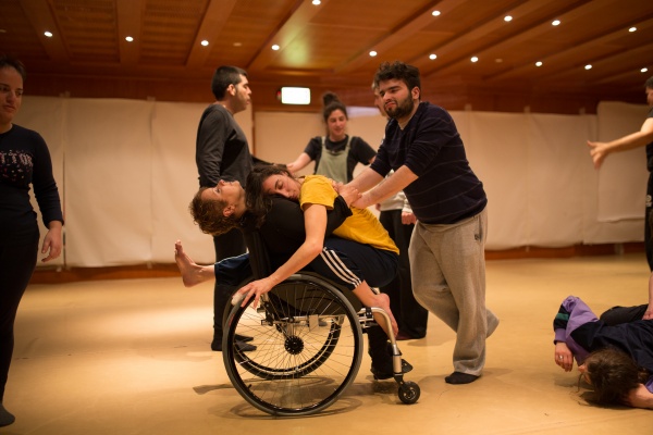 Photograph of a dance workshop featuring disabled dancers, one dancer is hugging another dancer in a wheelchair
