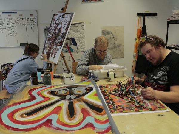 Three artists work closely on painting in a small studio