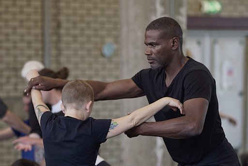 Two dancers duet, their arms outstretched, touching each other