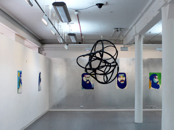 A black twisted cord suspended from the ceiling of an industrial white room with portraits on the walls.