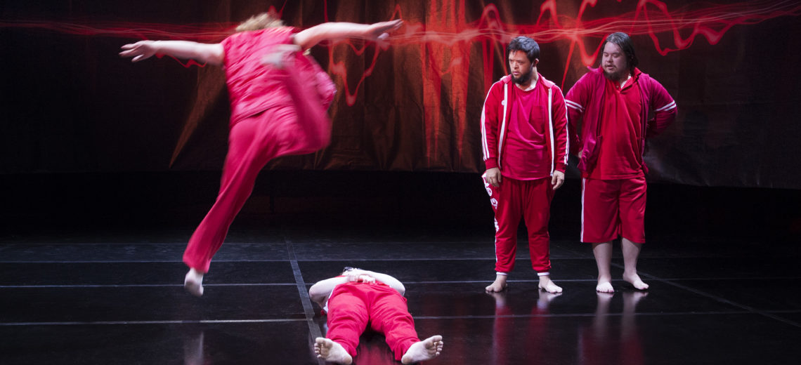 Four performers on a stage, all wearing red clothing. 