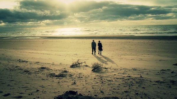 Screen grab showing two people walking on a beach