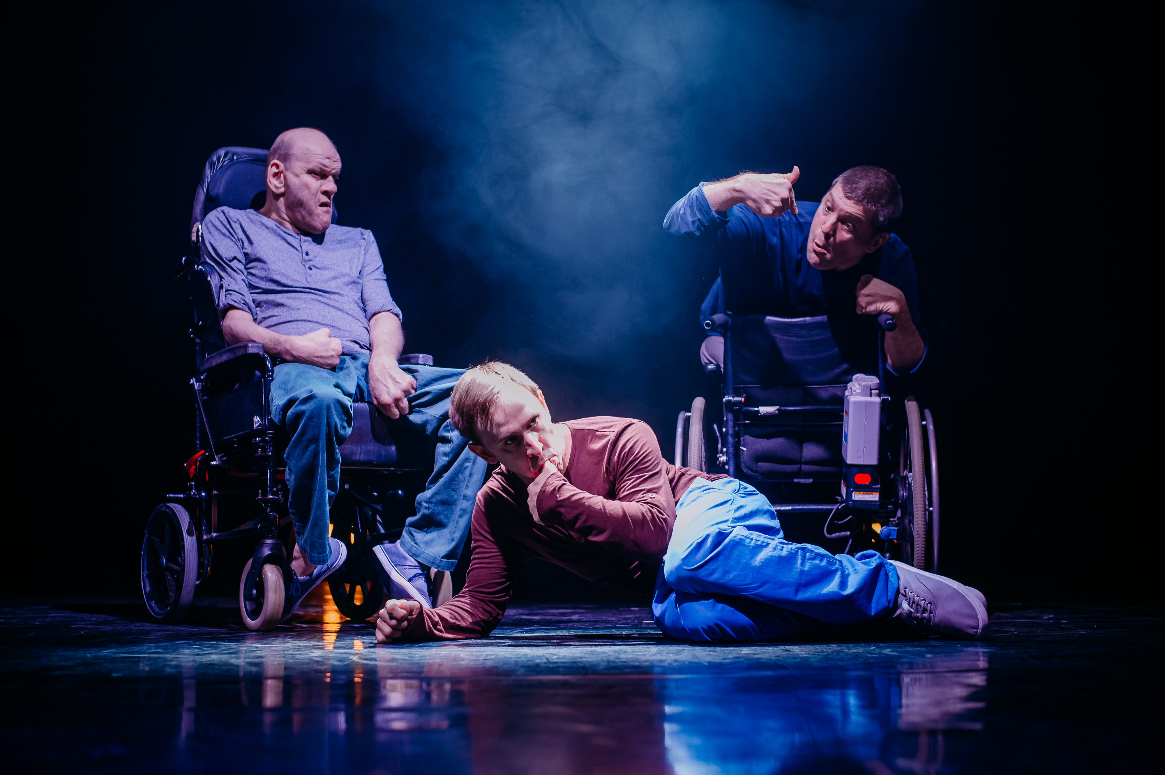 Man lying on ground, 2 men in wheelchairs behind him