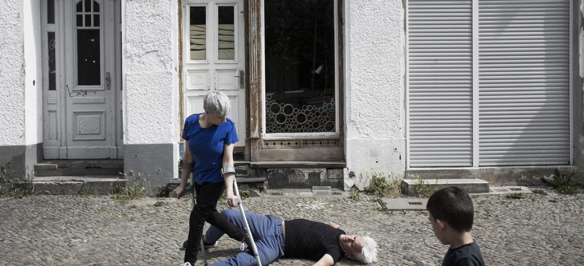 A woman with crutches walks over a man laying in the street