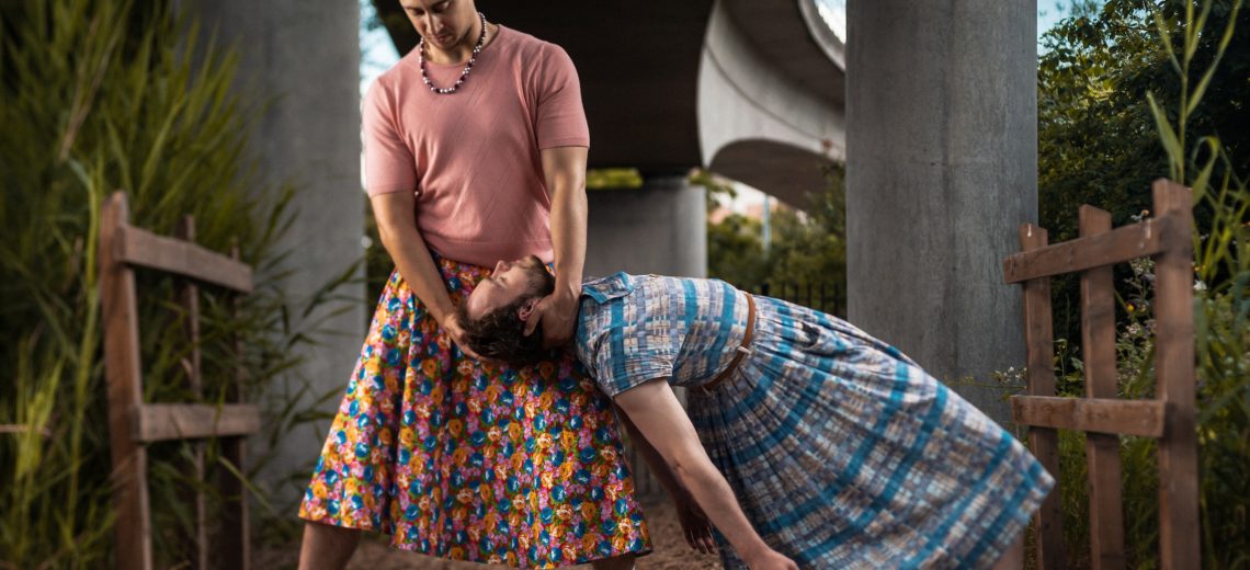 Two male dancers are holding onto each other, both dressed in dresses.