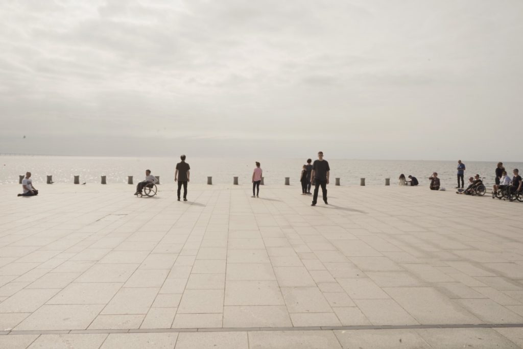 Group of performers standing in poses in front of the ocean
