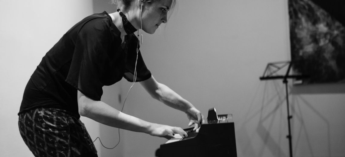 Female performer arches over her vintage toy organ with both hands on the keyboard.