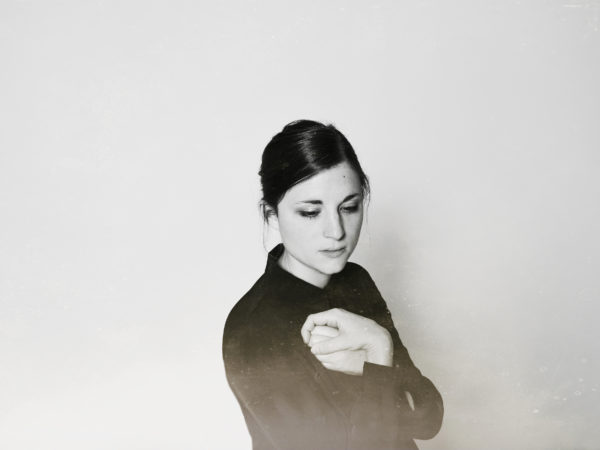 Black and white image of female with dark hair and black shirt clutching both hands together