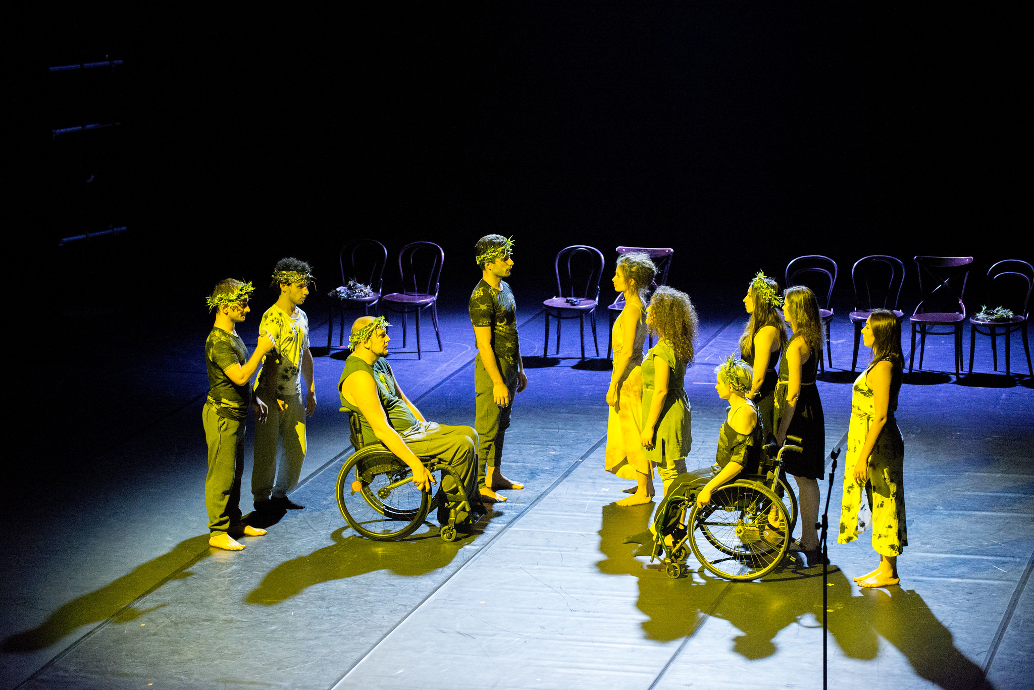 9 disabled and non disabled performers illuminated with yellow lights on a blak stage