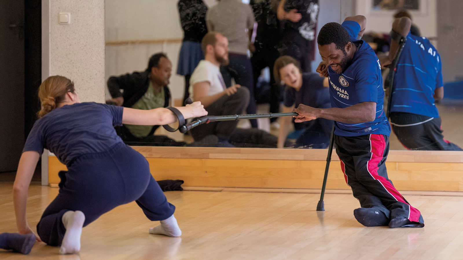 A black man and white woman take part in a dance masterclass using crutches