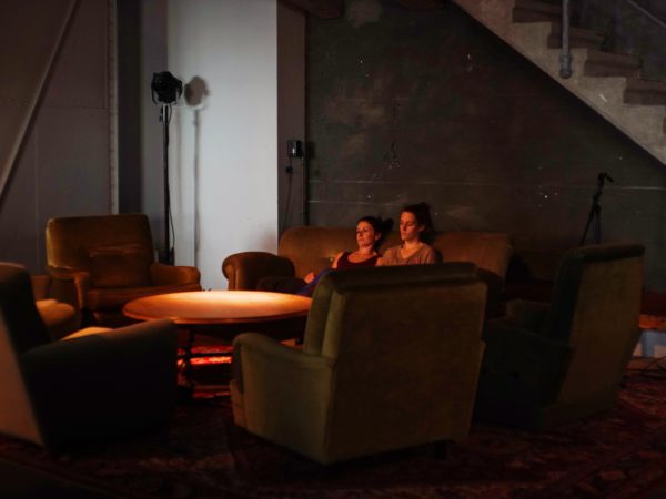 Two female performers sit on a sofa as they create a site-specific work